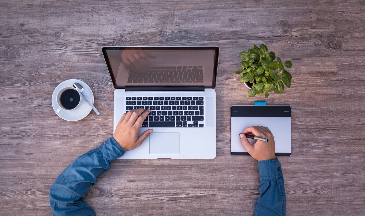 top view of a woman's hands typing on a laptop and a cup of coffee on a wooden